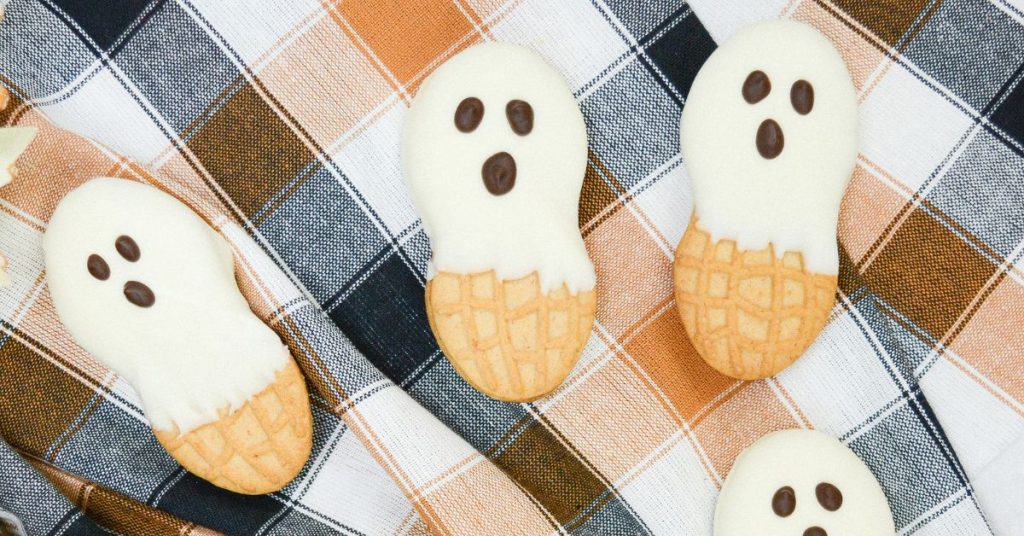 3 Nutter Butter Ghost Cookies on an orange and black plaid napkin.