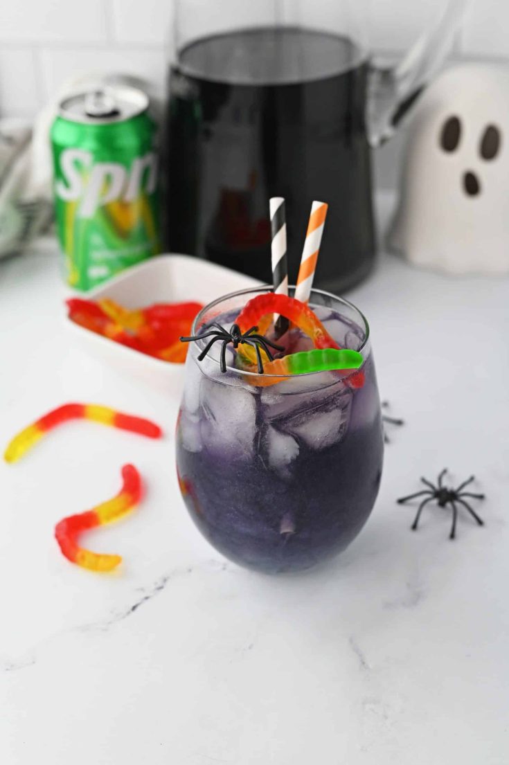 Purple Halloween Punch in a glass with gummy worms and plastic spiders. 