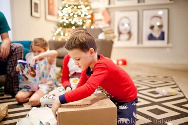 Boy opening his Christmas gift in the living room with family. One of his 7 gifts. 