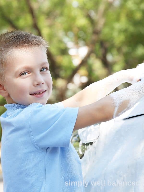 A young boy wearing a light blue shirt while washing his parent\'s car. 