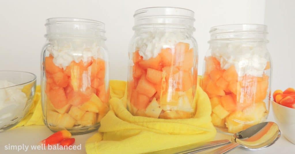 Cand corn parfait in a mason jar with pineapple, cantaloupe and topped with whipped cream. 