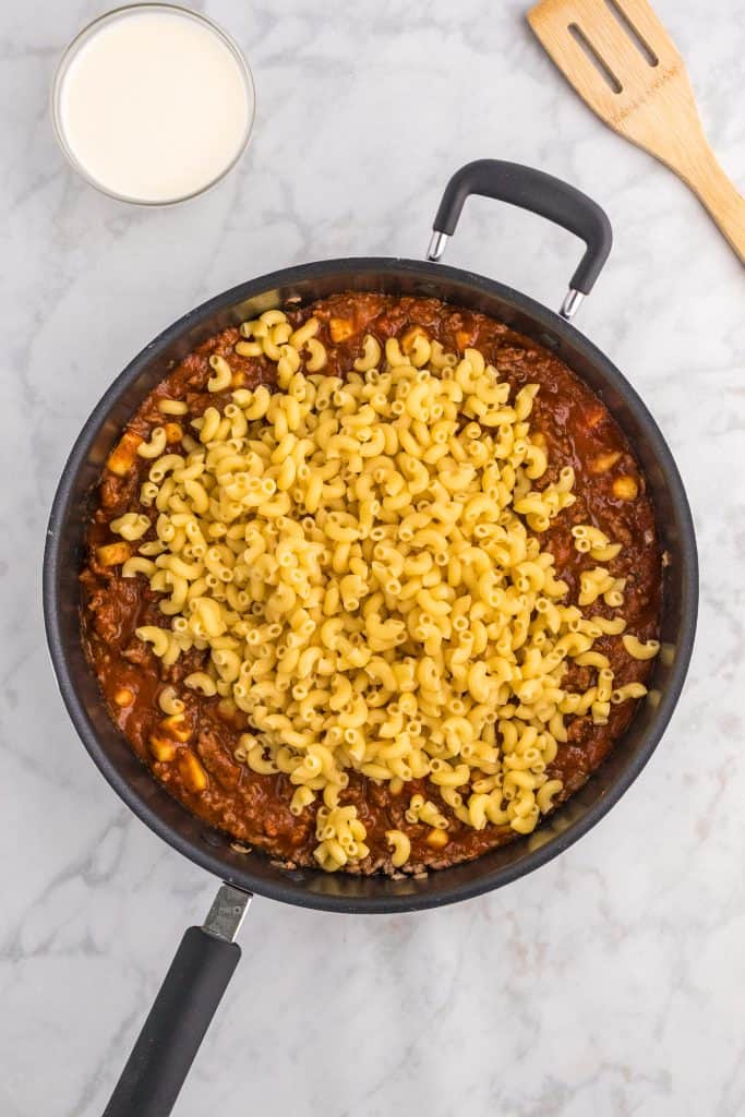 Macaroni pasta added to a pan of ground beef, zucchini, onions and sauce. 