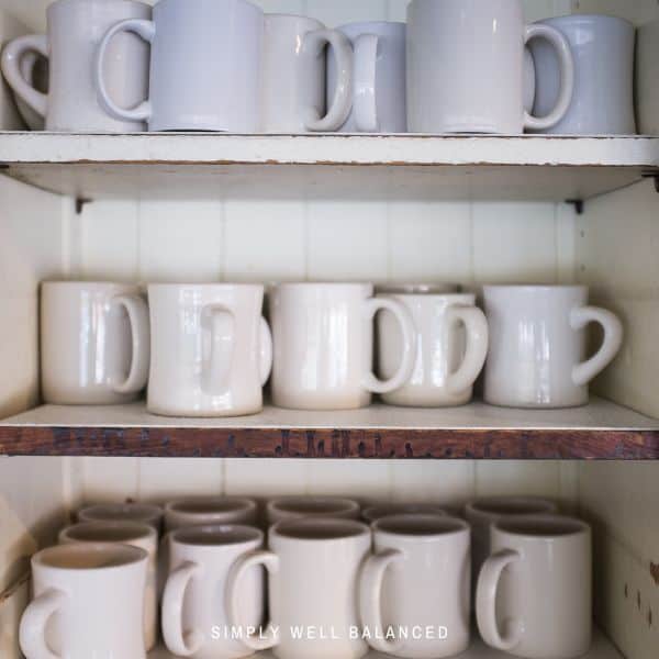 Collection of white coffee mugs in a kitchen cabinet.