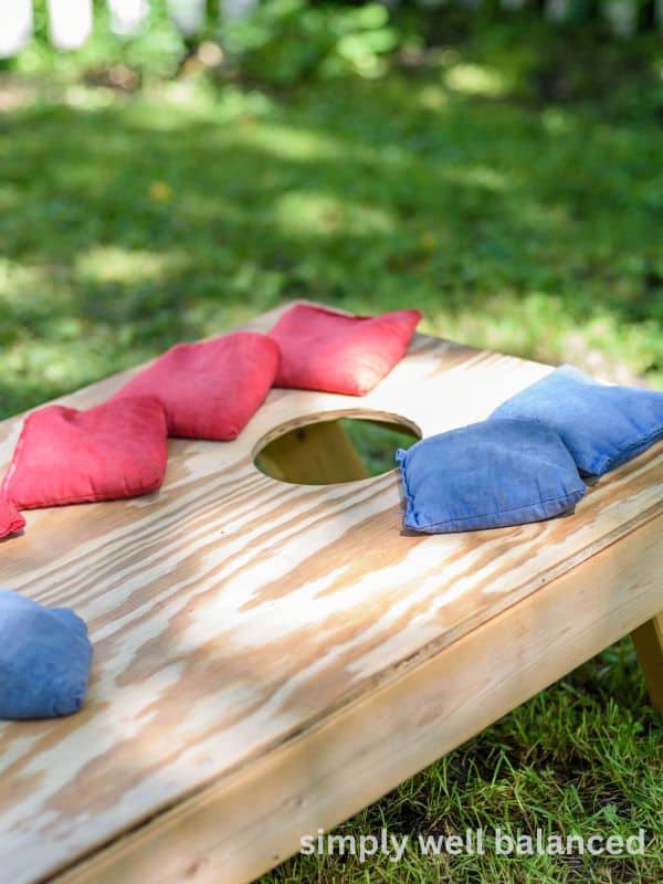 A wooden corn hole board with red and blue bean bags. Corn hole is a great screen-free activity to get kids outside during the summer. 