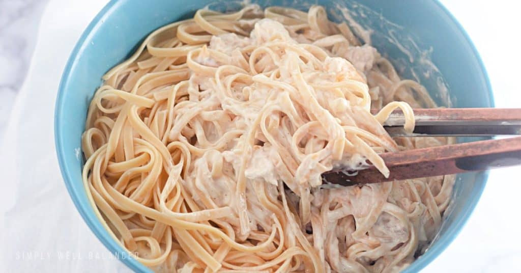 Tossing the cooked fetuccini with the sauce for the creamy chicken tetrazzini casserole. 
