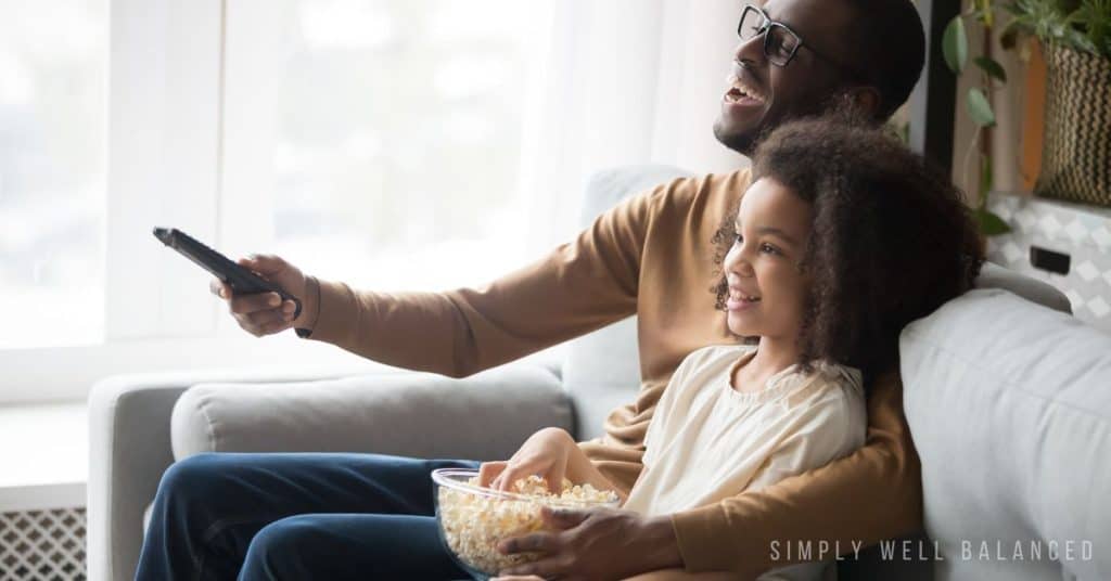Father and daughter doing a movie marathon and eating popcorn. 