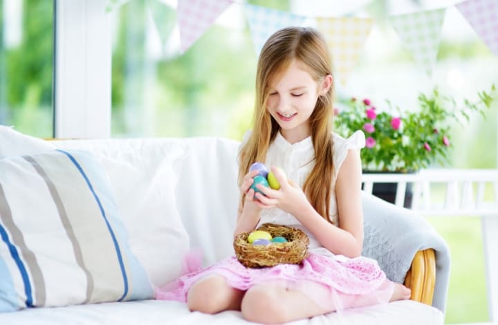 Little girl sitting on a bench holding Easter Eggs that were in a nest. 