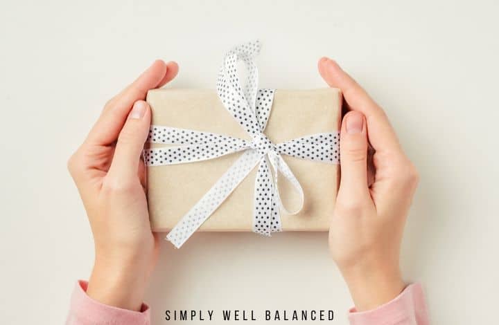 Close up image of women's hands holding a small gift wrapped in craft paper with a ribbon that is white with black polka dots.