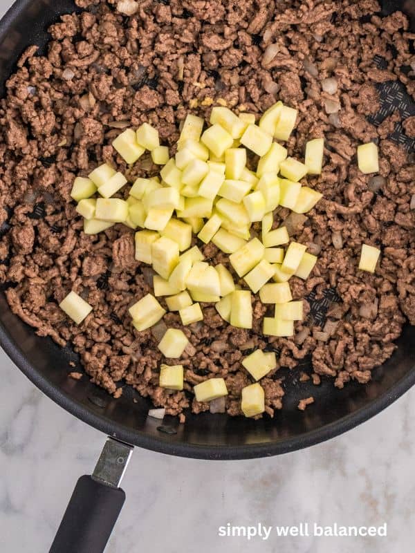 Diced zucchini added to ground beef and onions cooking in a pan. 