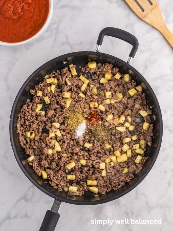 Spices added to a pan of ground beef, zucchini and onions. 