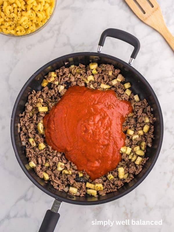 Pasta sauce added to a pan to make ground beef zucchini casserole. 