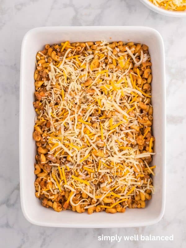 Zucchini casserole with ground beef in a white casserole dish topped with shredded cheese. 