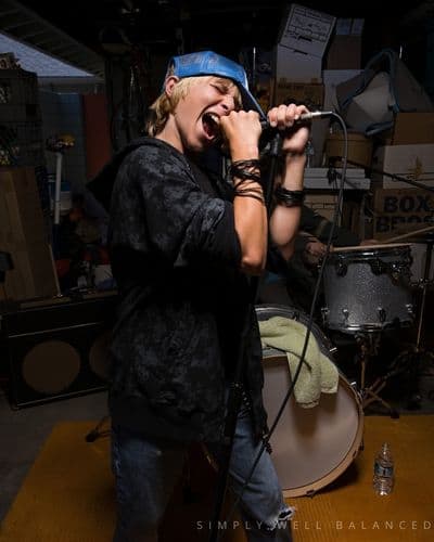 A tween boy wearing a hat and lip syncing into a microphone at a slumber party. 