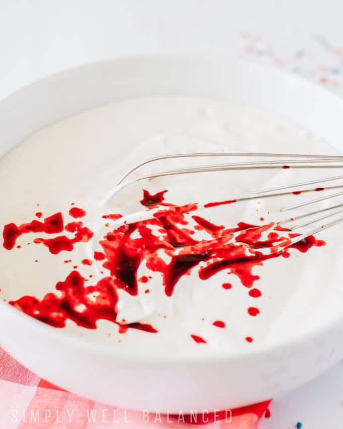 Drops of red food coloring on top of a bowl of cool whip. 