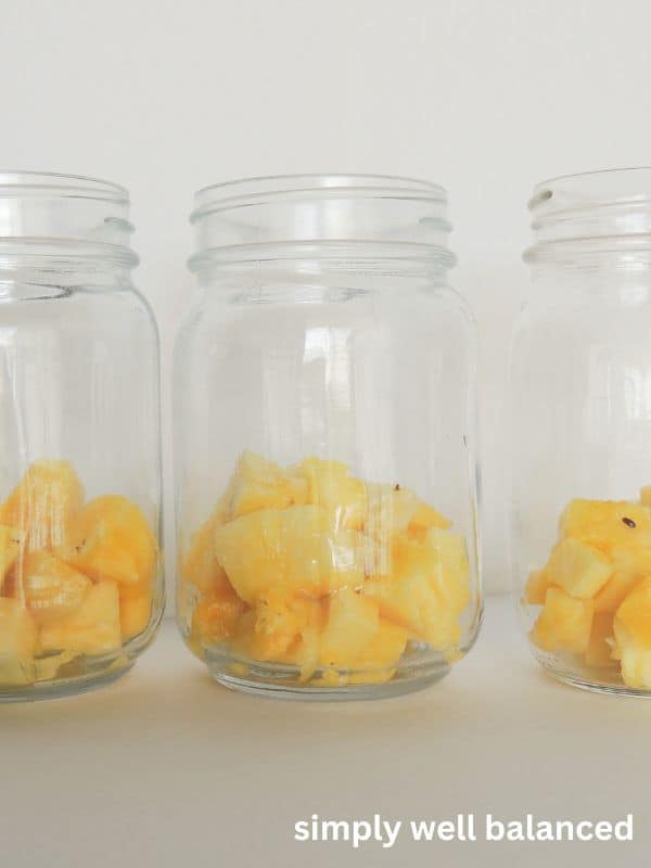 Glass mason jars with diced pineapple in the bottom. Layered Halloween parfait. 