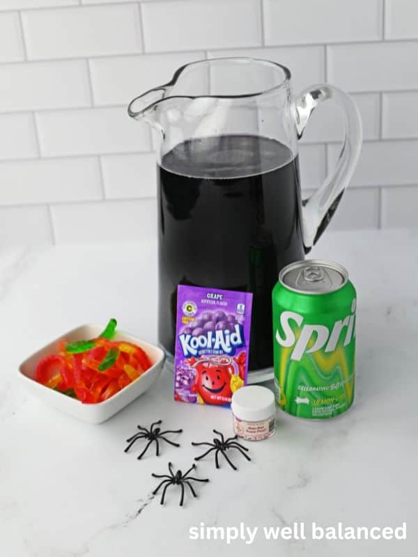 Ingredients for Purple Halloween Punch on a kitchen counter: Grape Kool-Aid, Sprite, Gummy Worms and Edible Glitter. 