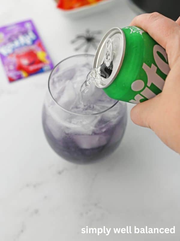 Hand pouring a can of Sprite into a glass to make Purple People Eater Halloween Punch. 