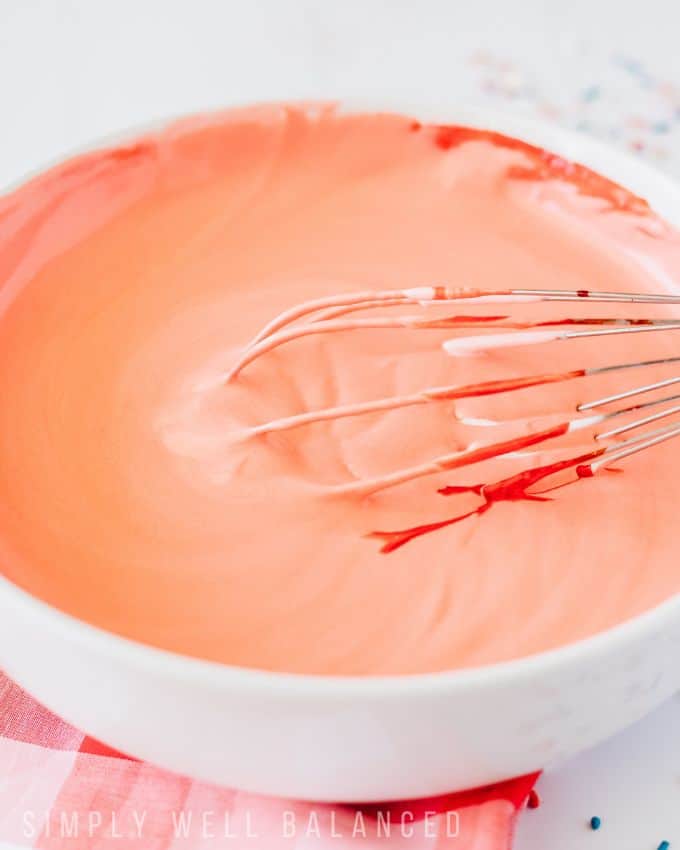 A bowl of red whipped cream being mixed with a whisk. 