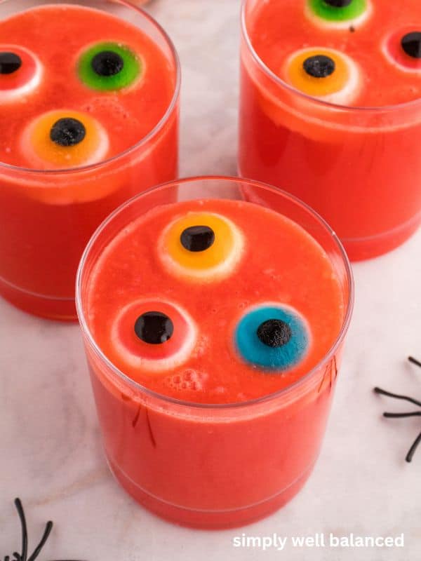 Three glasses of Halloween Hawaiian Punch with a black plastic spider nearby on the counter. 