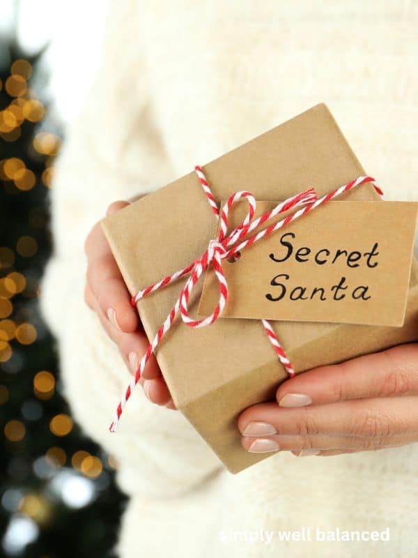 Woman holding a Secret Santa gift box wrapped in Kraft paper and tied with red and white string. 
