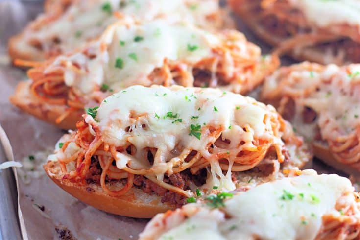 Close up of baked spaghetti bread with melted cheese and parsley garnish.