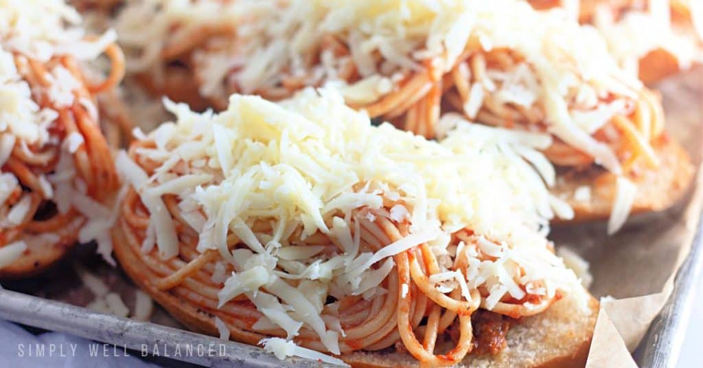 Baked spaghetti bread topped with cheese and ready to go back into the oven. 