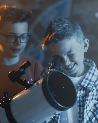 Two young boys look through a telescope at a sleepover party. 