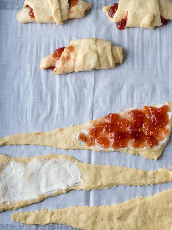 Crescent rolls being filled with a layer of cream cheese and strawberry jam. 